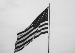 Monochrome image of the USA flag flying on a pole against a clear sky.